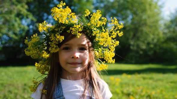 Portrait of a Little Girl in a Flower Wreath on Her Head Who Looks at the Camera and Smiles in the