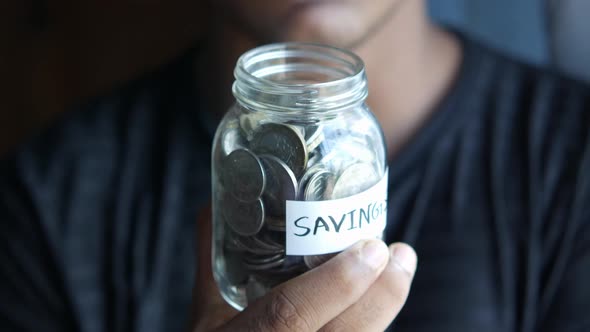 Young Man Hand Hold Saving Coins Jar