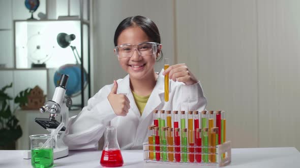 Young Asian Scientist Girl Looking At Liquid In Test Tube And Showing Thumb Up