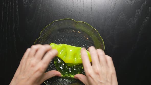 Female Fingers kneading a yellow transparent slime in a glass bowl.