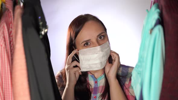 Close Up of Young Woman Putting on Medical Mask on Her Face, Standing Between Clothes in Wardrobe.