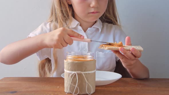 Child eating crispbread with peanut butter sitting at table home kitchen Girl with bread slice