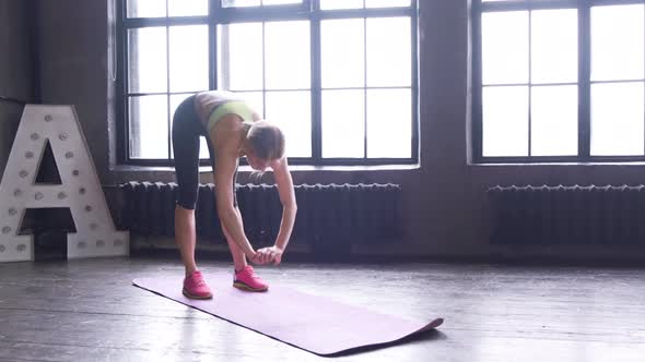 Woman doing stretching near a large window in a yoga room. Strength, training.