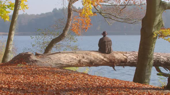 A Mid Aged Man is Waiting. He Looks over a Autumnal Lake.