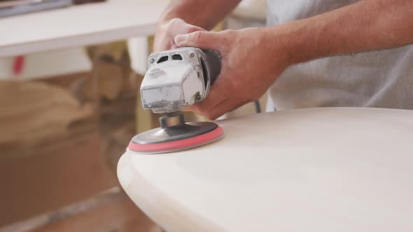 Caucasian male surfboard maker wearing a breathing face mask and shaping a wooden surfboard