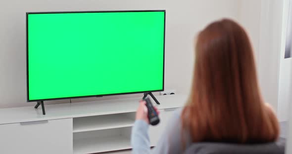 Girl Is Sitting on the Sofa in the Living Room and Watching TV, Green Screen, the Girl Switches