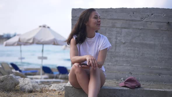 Excited Young Caucasian Woman Sitting on Summer Tourist Resort Laughing Looking Away