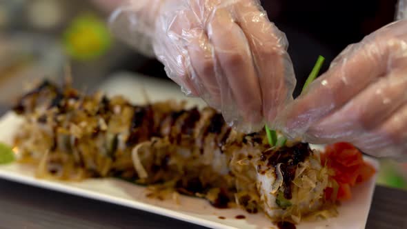 On the foreground we see a plate with sushi. On the background chef is doing some preparations and t