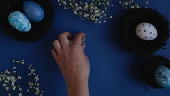 Top view of hands writing happy easter with the help of scrabble letters on a blue background surrou