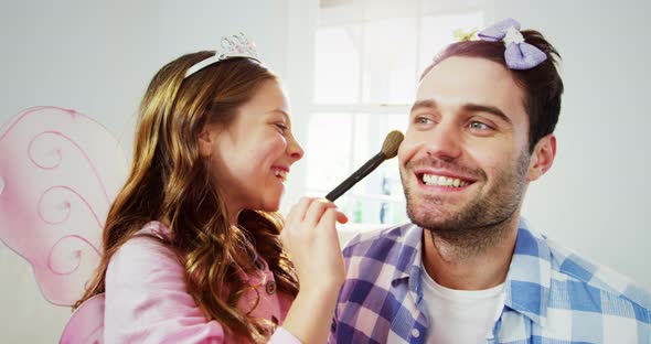 Girl dressed up in a fairy costume applying make-up on fathers face