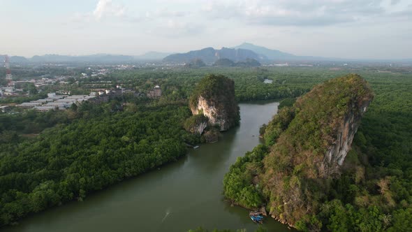 Aerial drone panning left over a river running between two large limestone mountain rocks (Khao Khan
