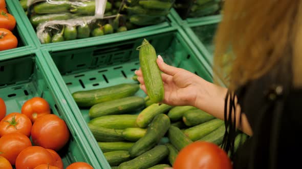Closeup of a Young Woman Choosing Cucumbers and Tomatoes in a Grocery Store
