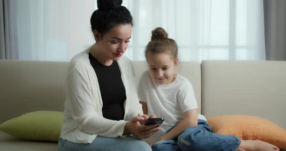 Happy Mom and Cute Daughter Little Kidmother Playing with Child at Home Relaxing Use a Smartphone