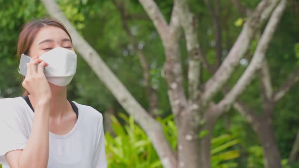 Asian sport woman wear mask, talking on mobile phone in public park.