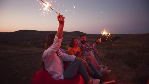 Happy Friends are Sitting with Sparklers on Bag Chairs