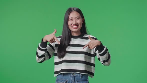 A Smiling Asian Woman Showing Gesture To Camera While Standing In Front Of Green Screen Background