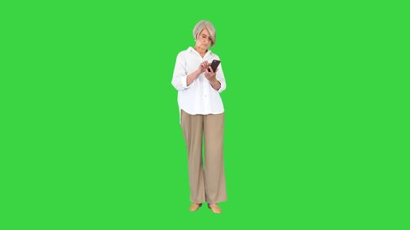 Stylish Mature Woman Typing Text Message on Mobile Phone on a Green Screen Chroma Key