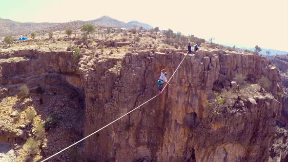 Aerial view of a woman balancing while tightrope walking and slacklining across a canyon.