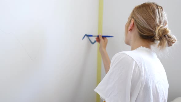 woman paints with blue paint on the wall of a room at home