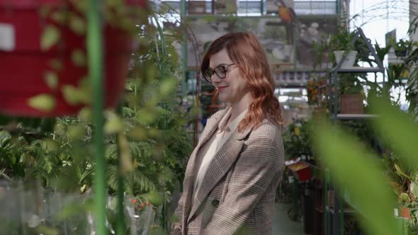 Female Customer in Glasses for Sight Chooses Flowering House Plants in Pots for Interior Decoration