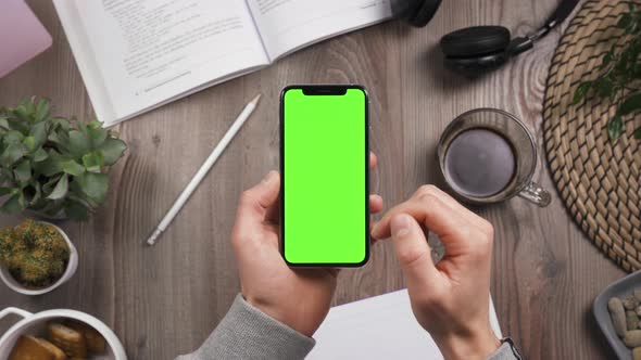 Top View. Phone in Hands, Swipe Up on Green Screen. Chroma Key. Workplace Table.