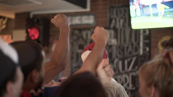 Football fans excitedly cheering while watching televised match at sports bar