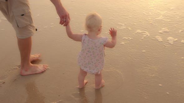 Unrecognizable Caucasian Caring Father Holding Baby Daughter Toddler By Hand Stepping Walking on Wet