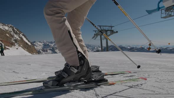 Woman Putting On Skis On Ski Slope By Cable Cars