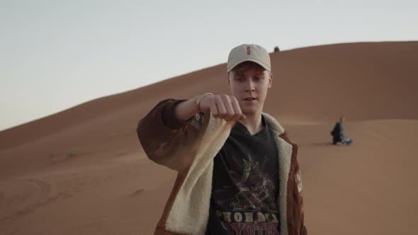 Adult Caucasian Man Playing with Fine Sand on Desert Pouring It From Hand and Letting It Drift in