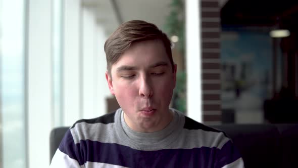 A Young Man Is Eating a Burger. A Man Sits in a Cafe By the Panoramic Window and Eats Fast Food.