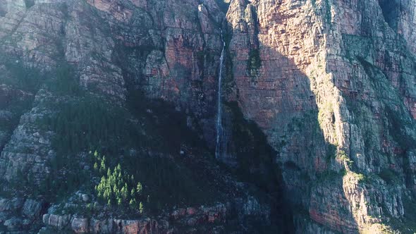 Aerial - Ascending drone reveals beautiful waterfall dropping from sheer cliff of imposing sandstone