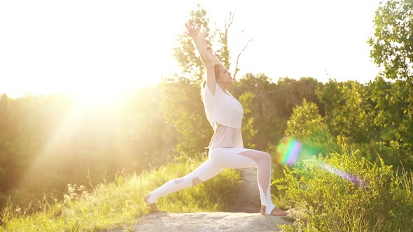 Young Woman Is Practicing Yoga and Performing Warrior Pose in Evening on Background of Sunlight
