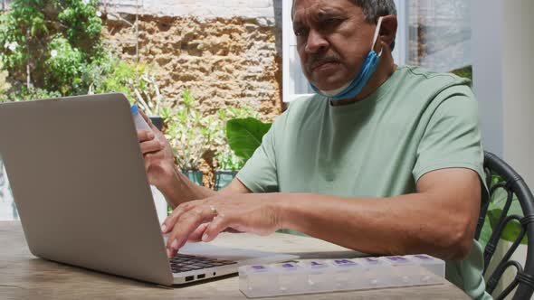 Senior mixed race man wearing lowered face mask having medical consultation using laptop