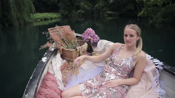 Pretty Woman In Glittery Dress Sitting On A Boat Floating In The Calm Lake - medium full shot