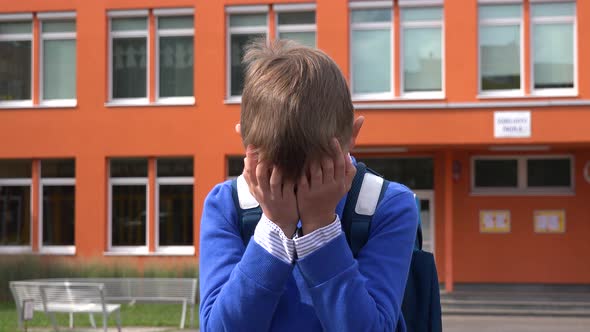 A Young Boy Uncovers His Eyes and Looks Around in Confusion - an Elementary School in the Background