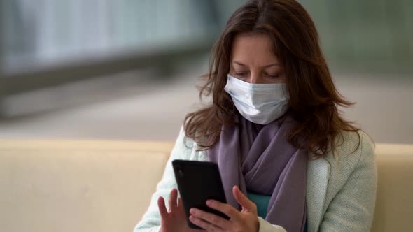 Woman with Facial Mask for Protecting From Coronavirus Is Using Smartphone in Public Place, Waiting