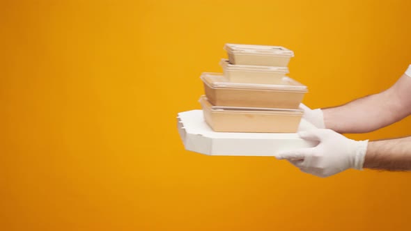 People's Hands Passing Each Other Packed Boxes with Food Delivery Against Yellow Studio Background