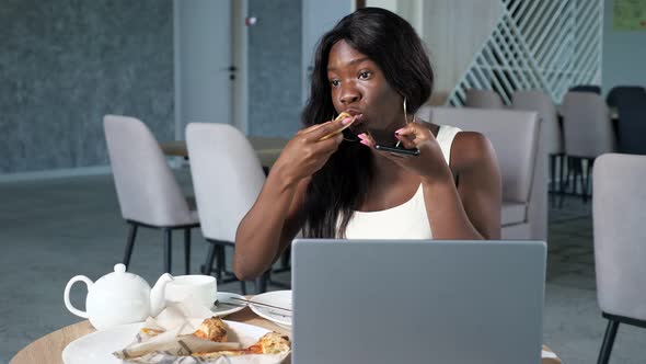 Young Black Woman Eats Pizza Talking on Phone in Cafe