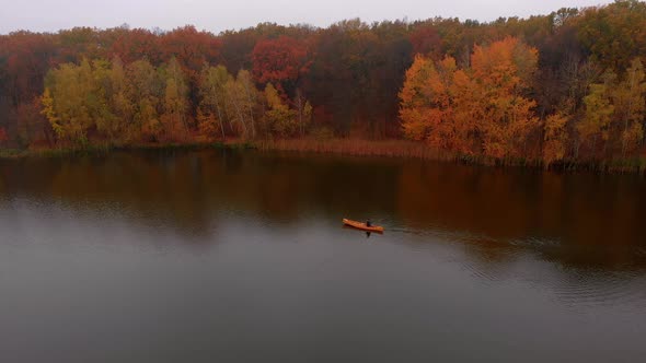 Man Is Floating in Yellow Boat Canoe on the River Near Colorful Trees at Golden Autumn