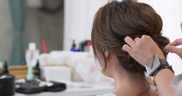 Female hairdresser standing and making hairstyle on bride in beauty salon