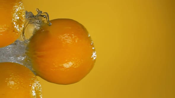 Ripe Oranges are Bouncing Horizontally with Water Splashes on Yellow Background