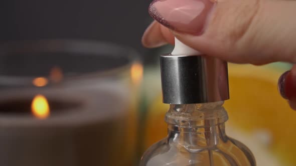 Essential Oil Drips From a Pipette Into a Bottle on the Background of a Candle