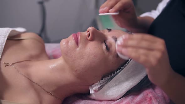 Closeup View of Professional Cosmetologist is Cleaning Woman's Face Using Cotton Sponge