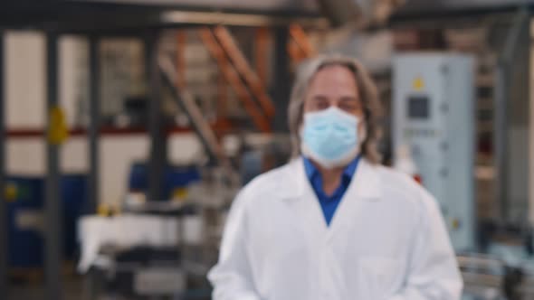 Senior Chemical Industry Worker in Coat and Safety Mask Putting on Plastic Glasses Looking at Camera