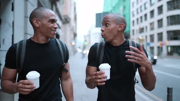 Two cheerful bald African brothers talking and walking with cups of coffee on the street