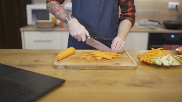 Young Man in Apron Chopping Carrots for Christmas Dinner