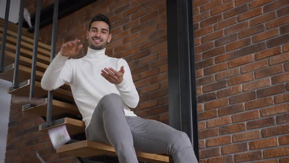 Rich Laughing Young Middle Eastern Man Scattering Cash Money Sitting on Stairs in Luxurious Home