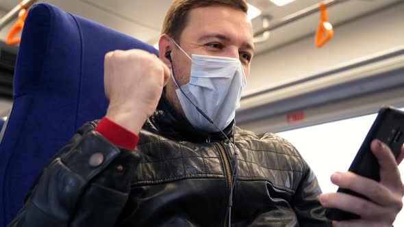 Excited Male Wearing Medical Face Mask Looks at Phone and Celebrates Big Win Financial Good News