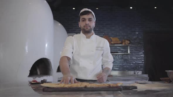 Portrait of Chef in White Uniform Demonstrating Freshly Baked Fatayer Lying on the Wooden Board