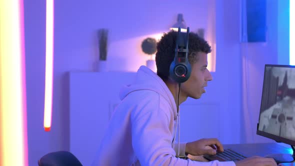 Medium Shot of Young Black Gammer in Headphones Playing in Online Shooter